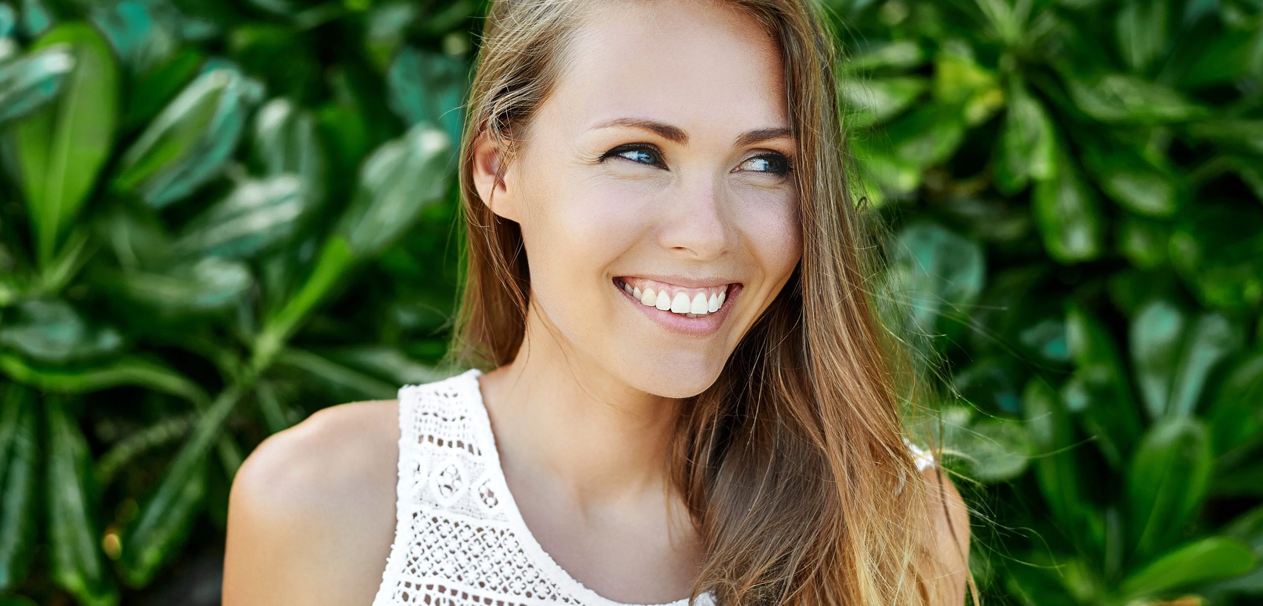 Woman with glowing skin smiling with green palm leaves behind her