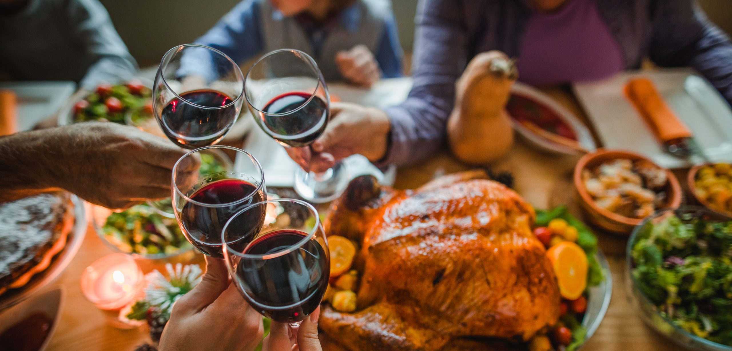 People cheers-ing with glasses of red wine over a roast dinner